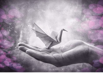 Main ouverte tenant un oiseau en origami, en noir et blanc avec touches rose et violet.