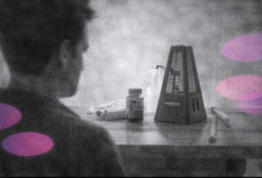 Personne seule observant un métronome électronique posé sur une table, en noir et blanc avec accents rose et violet.