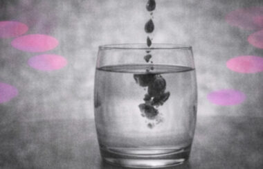 Gouttes d’encre noire tombant dans un verre d’eau claire, en noir et blanc avec accents rose et violet.