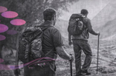 Un guide et un randonneur avancent sur un sentier montagneux en noir et blanc, côte à côte.