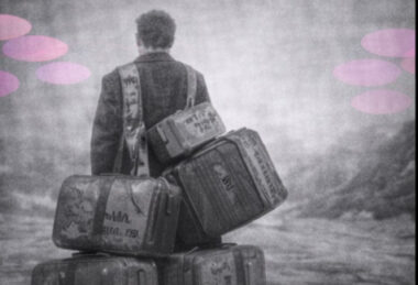 Personne portant plusieurs valises anciennes avec des initiales familiales, en noir et blanc.