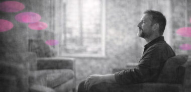 Personne assise dans un cabinet lumineux, des ombres s’estompant autour d’elle, en noir et blanc avec accents rose et violet.