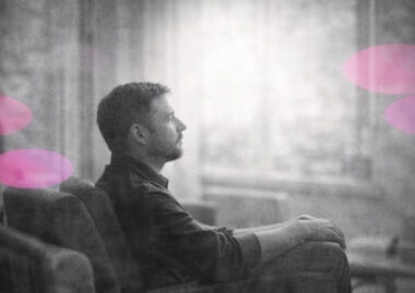 Personne dans un cabinet, debout près d’une ombre, en noir et blanc, avec accents rose et violet en arrière-plan.