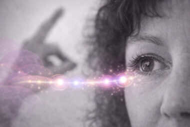 Gros plan d’un œil en noir et blanc suivant un mouvement de la main en arrière-plan, avec une ligne de stimulations lumineuses rose et violet illustrant les mouvements alternatifs en TLMR